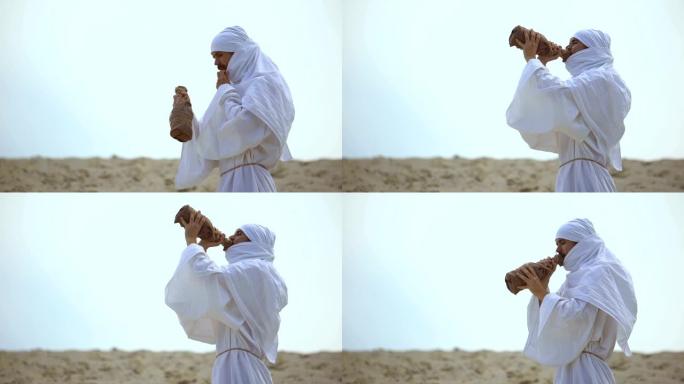 干渴的阿拉伯朝圣者从沙漠中的瓶子喝水，干旱问题