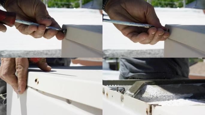 一名高加索杂工使用平头螺丝刀从屋顶沼泽冷却器上卸下生锈的螺钉，并在晴天打开顶部