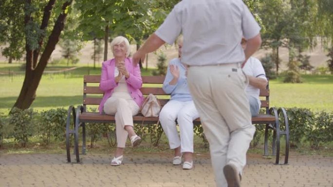 三名高加索老人坐在长凳上，为他们开朗的男性朋友跳舞鼓掌