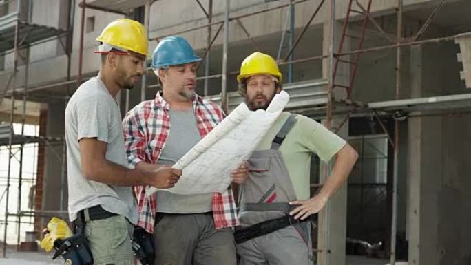 建筑工人在施工现场看着外面的平面图，并指向建筑物上的细节