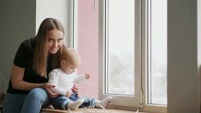 母亲和她的宝贝儿子在家里玩得开心。1岁的小孩在一扇大窗户附近的家中与妈妈玩耍