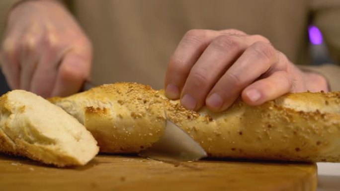 用锋利的钢刀切开新鲜出炉的脆皮面包特写，食物