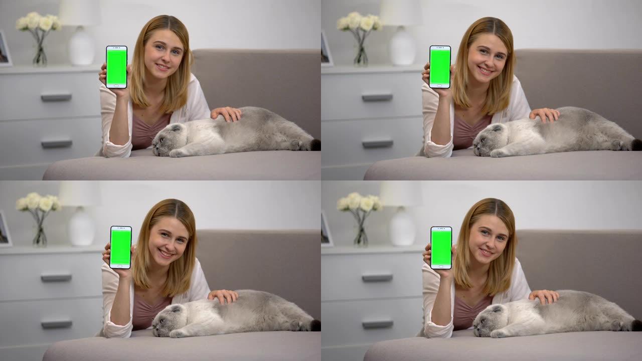 开朗的女孩，拿着猫的智能手机，动物慈善网站的绿屏
