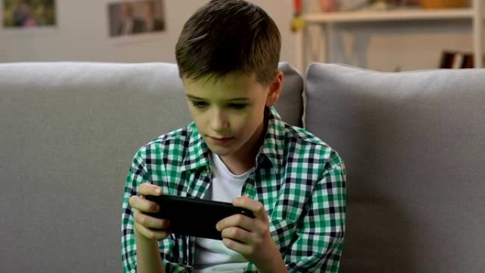 男孩在家玩智能手机上的视频游戏，年轻时的小工具成瘾