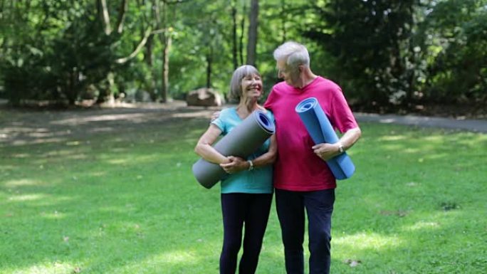 充满爱心的老年夫妇在公园里拿着运动垫