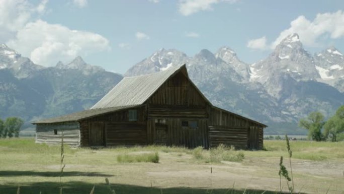 在阳光明媚的日子里，一个古老的木制小屋/谷仓坐落在怀俄明州西部大提顿国家公园的大提顿山脉的底部