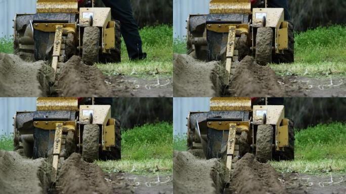 一个泥泞的挖沟机的慢动作镜头将一条沟渠切成室外的草地