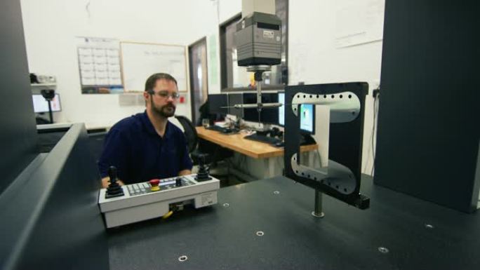 三十多岁的高加索技术人员使用带有红宝石红色火炬探针的坐标测量机来测量制造工厂中零件的公差