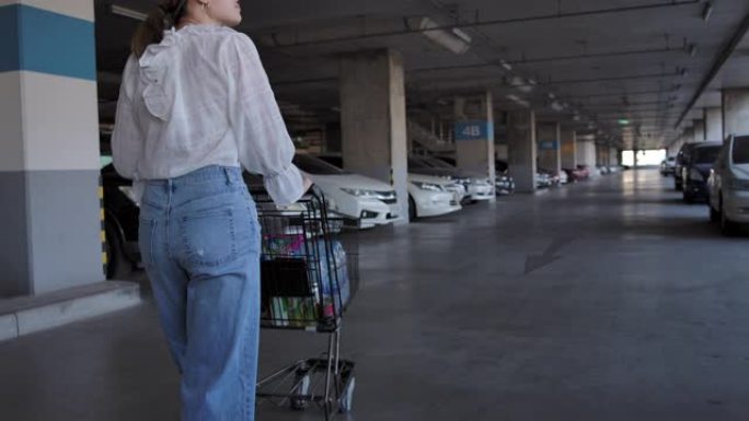 亚洲妇女购物拖着购物车到停车场。