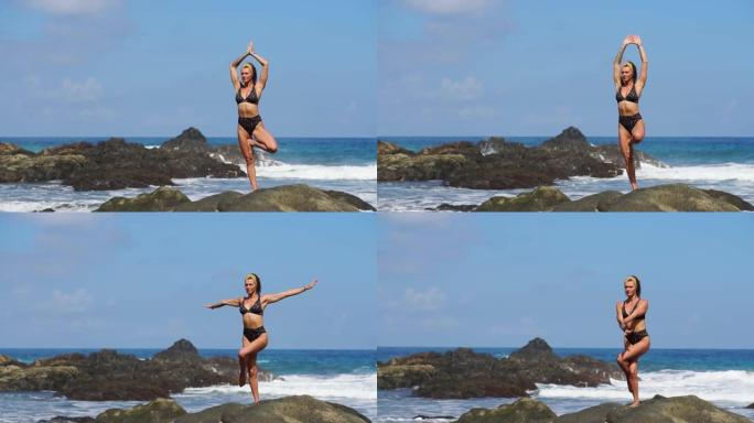 穿着比基尼平衡的年轻女孩站在一条腿上做瑜伽，站在海边的一块岩石上，黑沙。通过放松冥想。体操