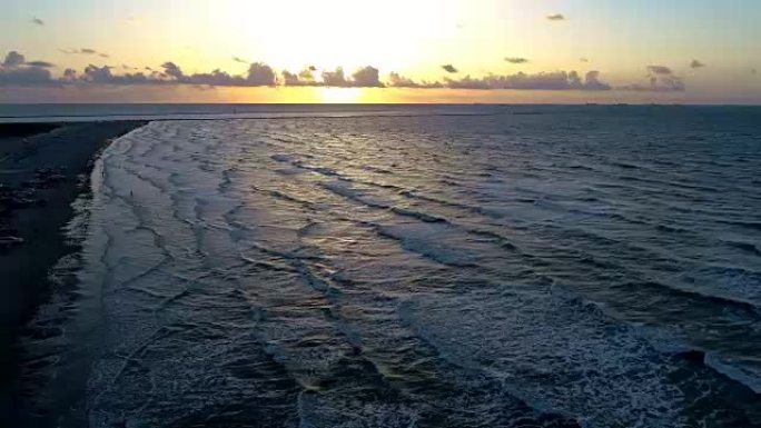 在海洋上令人惊叹的日出期间，沿着墨西哥湾的帕德里岛海岸线，沿着海滩和水直升起无人驾驶飞机