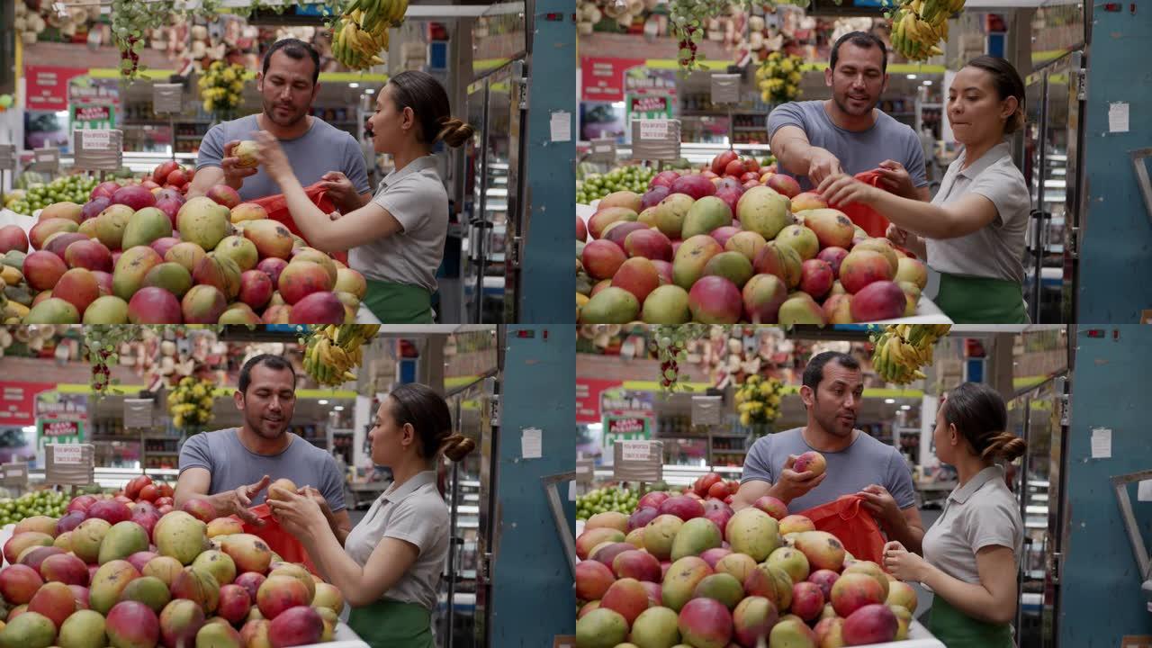 在农贸市场上的拉丁美洲女售货员帮助客户选择芒果，同时将芒果添加到可重复使用的袋子中