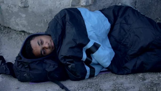 非洲男性难民躺在街道上，上面铺着睡袋，无家可归