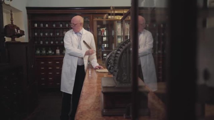 穿着白袍的白人男子用羽毛笔书写的侧视图。药剂师呆在收银台修改他的钞票。复古药店、制药博物馆。