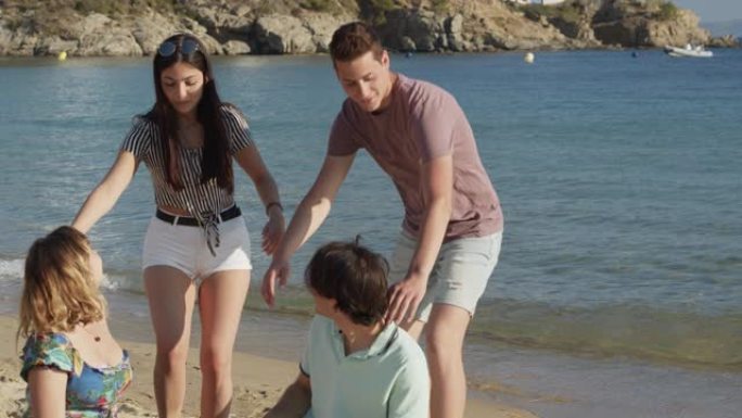 年轻夫妇手拉手在西班牙海滩上与朋友同行