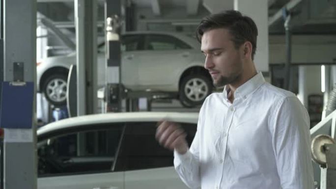 年轻英俊的汽车服务男子扔起他的车钥匙，在他的汽车背景上微笑