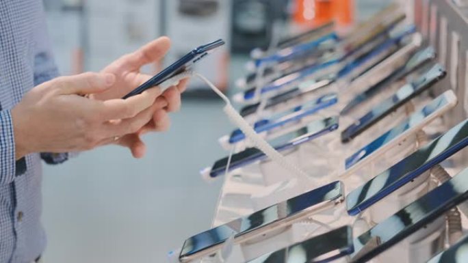 一个男人的手的特写镜头正在选择在一家电子商店的店面附近购买新的智能手机