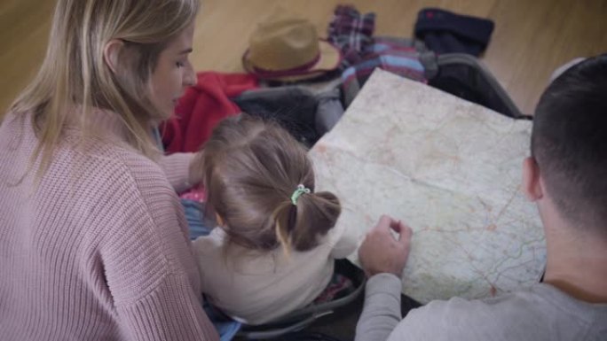 年轻的高加索家庭看地图的后顶视图。友好的父亲、母亲和女儿为旅行路线。旅游。生活方式，幸福。