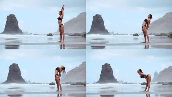一个美丽的女人在海洋海滩上，黑色的火山沙进行体操练习，练习健康的生活方式和户外训练。健身训练