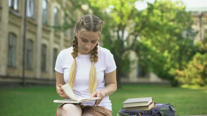 年轻女子在校园的长凳上读书，准备作业，教育