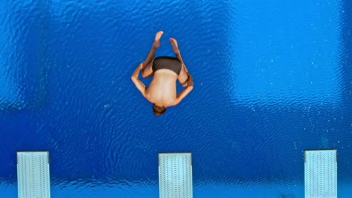 一名男性潜水员在阳光下潜入游泳池时旋转的SLO MO CS上方