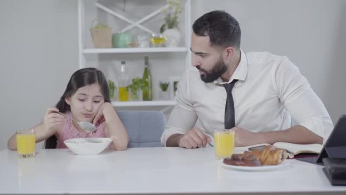 匆忙的中东商人和吃早餐的小女孩聊天，指着手表。父亲要求女儿快点。无聊的孩子没有食欲。家庭关系，生活方