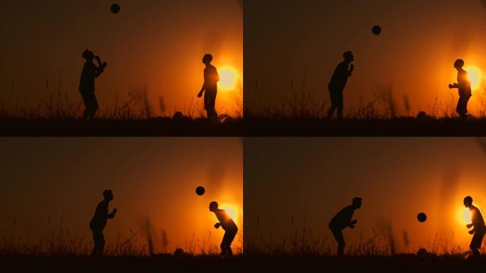 日落时两个男孩踢足球。儿童在日落时玩球的剪影。幸福家庭的概念
