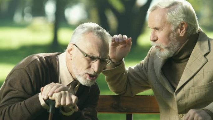 有听力问题的老年养老金领取者，坐在公园长椅上听朋友说话
