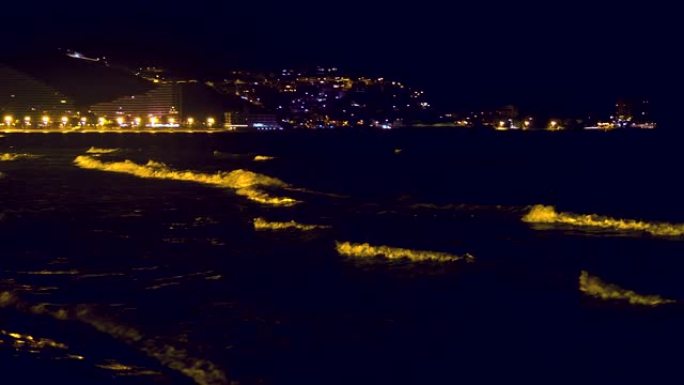 晚上，带有明亮白色波峰的海浪在西班牙度假城市上岸