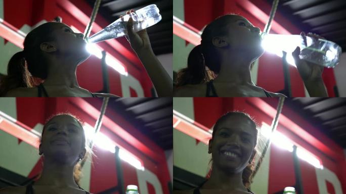 非裔美国妇女在健身房喝水，然后面对镜头微笑
