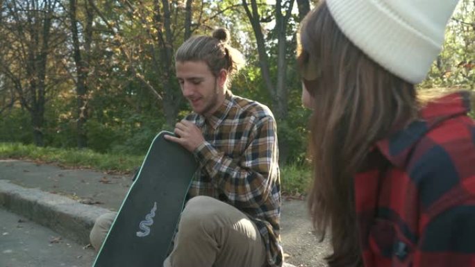 男孩和女孩坐在公园里交流。年轻的滑板运动员夫妇花时间在户外。
