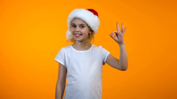 可爱的少女戴着圣诞老人帽子，显示ok标志和微笑，推荐