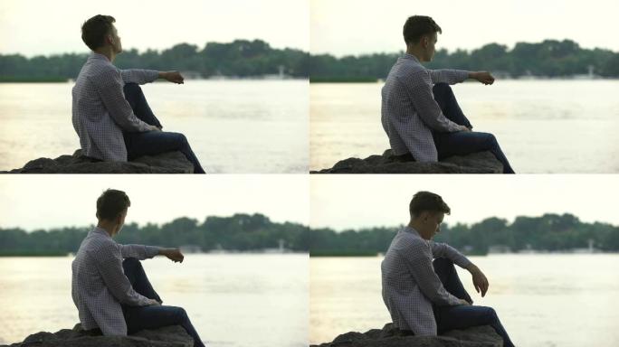 忧郁的男性青少年独自坐在河边的石头上思考生活