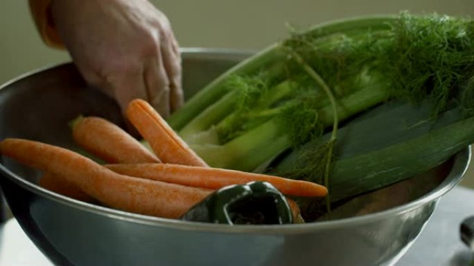 一位年长的白人妇女从砧板上捡起蔬菜，然后将其放在金属碗中。