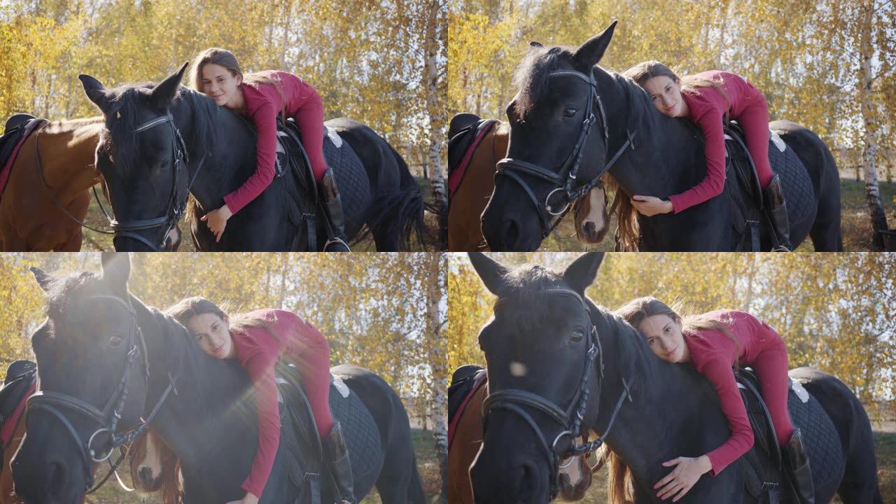 年轻的高加索女性马术者躺在马背上爱抚她的宠物。优雅的黑马站在秋天的森林中，年轻的骑手在他的背上。