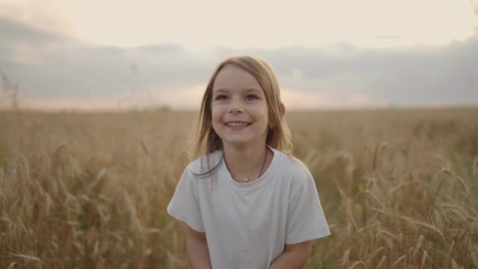一个快乐微笑的小女孩看着镜头慢镜头跑在麦田里，夕阳西下