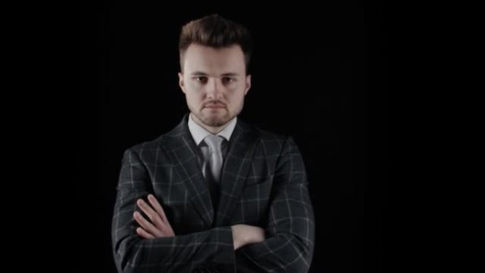 英俊自信的商人穿着西装，双臂交叉在黑色背景上。严肃的年轻白人男子胡子的肖像穿格子西装西装看相机