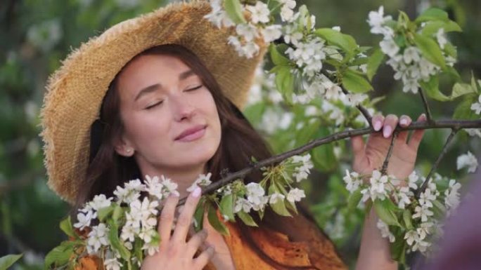 迷人的绿眼女士戴着草帽，闻着盛开的樱桃树枝，画像