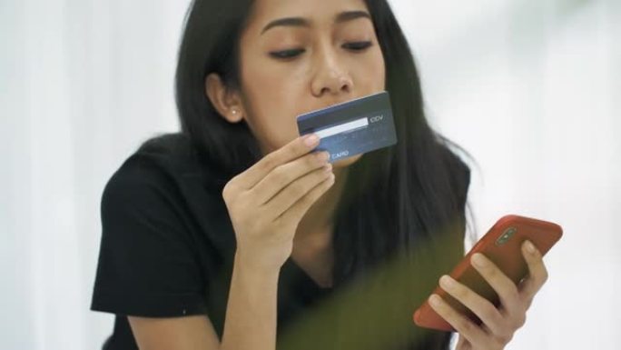 亚洲女性在床上用电话和信用卡在线购物