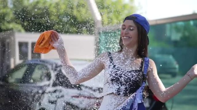 年轻快乐的女人笑着洗车洗发水在户外慢动作喷洒在身上。中枪快乐无忧无虑的高加索员工在阳光下洗车服务中享