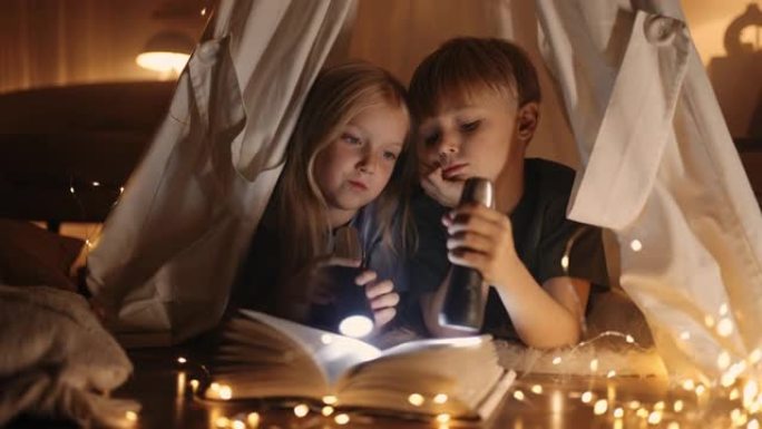 白人儿童晚上在家玩耍，男孩和女孩躺在帐篷里看书