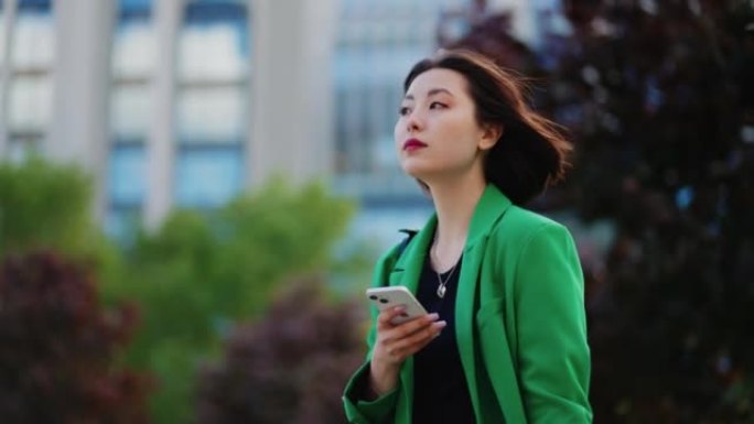 有魅力的韩国女人在城市公园等人，用智能手机上网，肖像