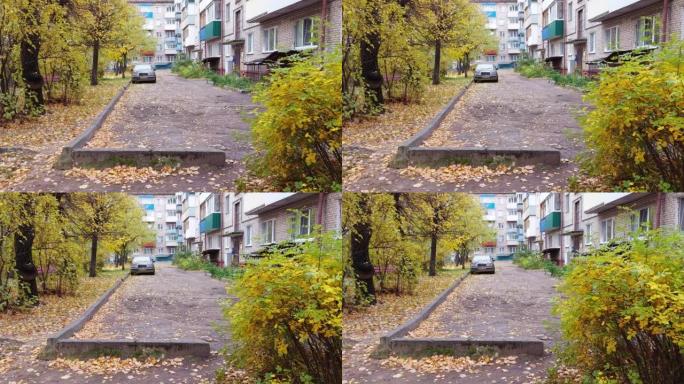 一幢多层住宅的院子里停放着汽车。沥青和道路上的水坑。黄色的树冠。一年中的秋天。