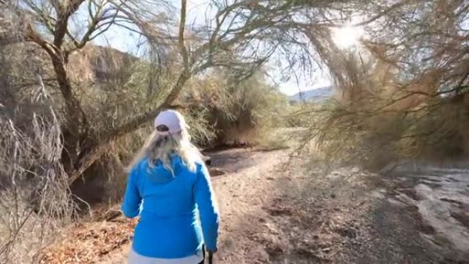 女性徒步旅行者沿着沙漠小径，在树下