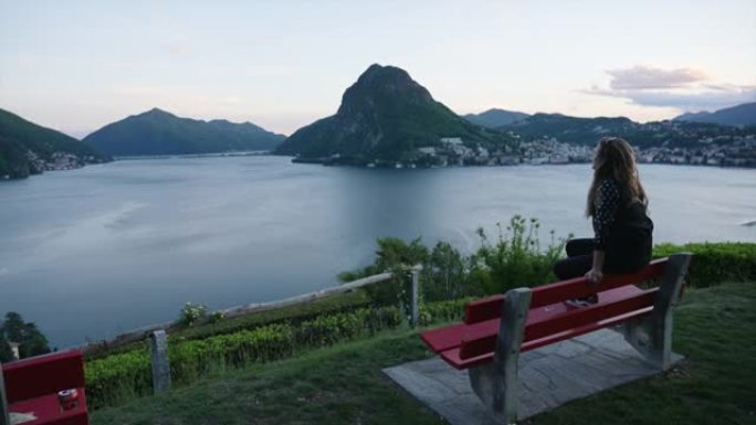 女人坐在长椅上，使用智能手机俯瞰城市和山脉