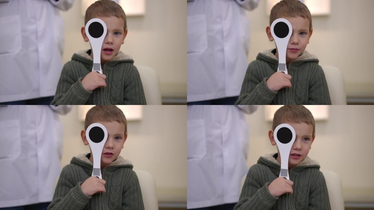 可爱的迷人的高加索男孩的肖像闭上了一只眼睛，眼睛被封堵器读着说话。在室内医院接受眼科检查的儿童的前视