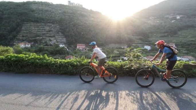 成熟的山地自行车夫妇在日落时沿着山路走