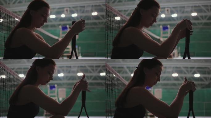 年轻的运动女子在比赛或训练后坐在网球场的地板上，扭动球拍，肖像射击