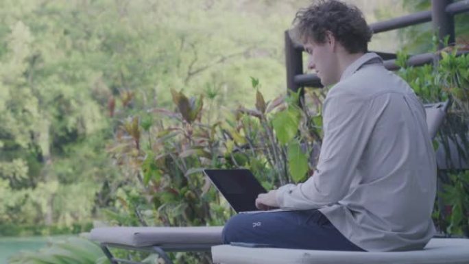 一名男子在花园附近使用笔记本电脑的详细照片