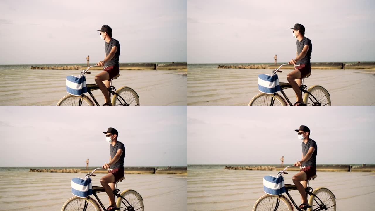 年轻人戴着口罩在海滩上骑自行车穿过退潮